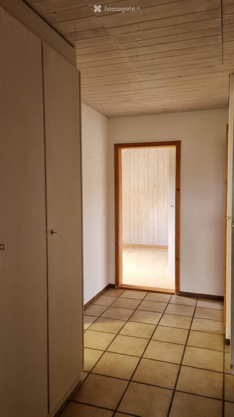 Empty room with tiled floor, wooden ceiling, white walls, wooden door, and a door leading to another room