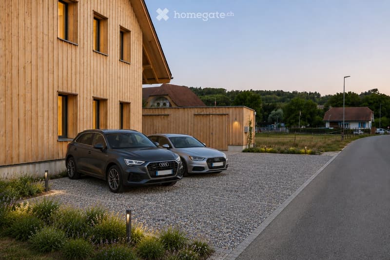 Modern wooden house with large windows and a sloped roof, two parked cars in front, surrounded by greenery and a rural landscape.
