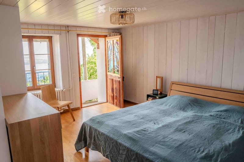 Cozy bedroom with wooden walls and floor, a large bed with blue bedding, a wooden chair, a small table with a mirror, and a radiator near the window.