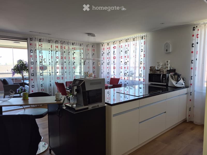 Modern kitchen with white cabinets, black countertops, coffee machine, microwave, blender, and a small dining area with a table and chairs.