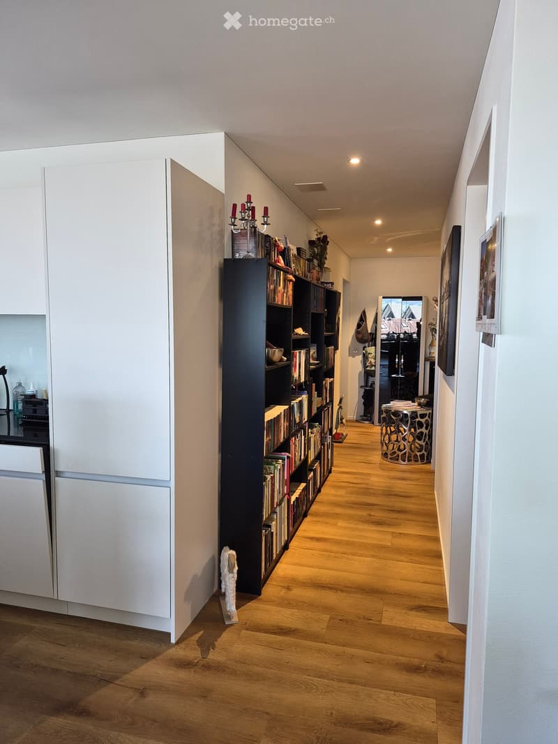 Modern hallway with wooden flooring, white walls, built-in storage unit, bookshelf, and decorative items.