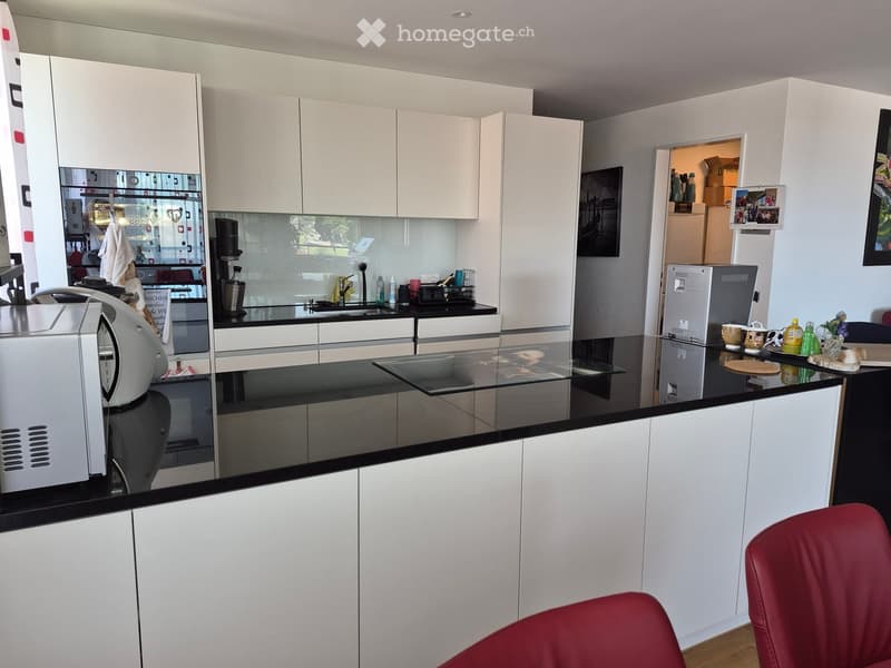 Modern kitchen with white cabinets, black countertops, a coffee machine, a refrigerator, and a sink area.