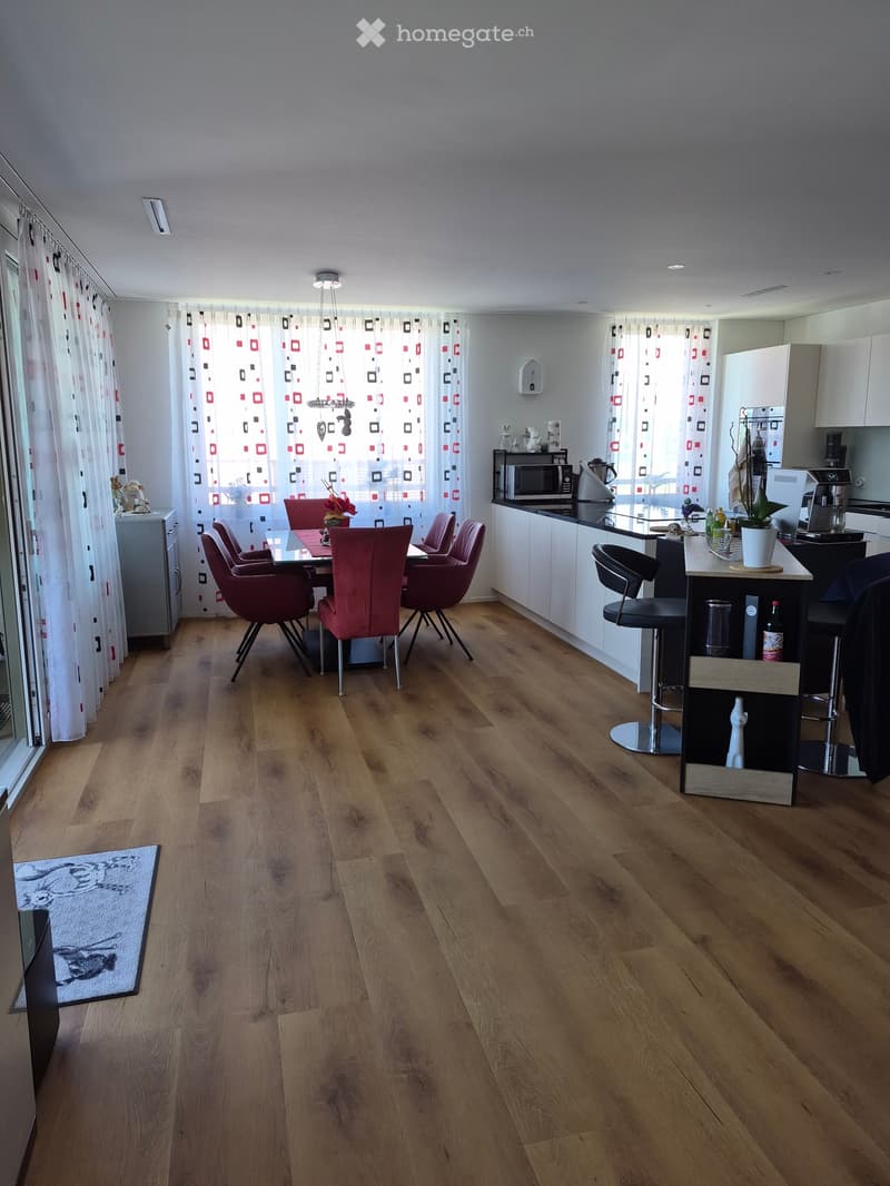 Open-plan living and dining area with wooden flooring, white cabinets, a dining table with chairs, and a kitchen island with stools.