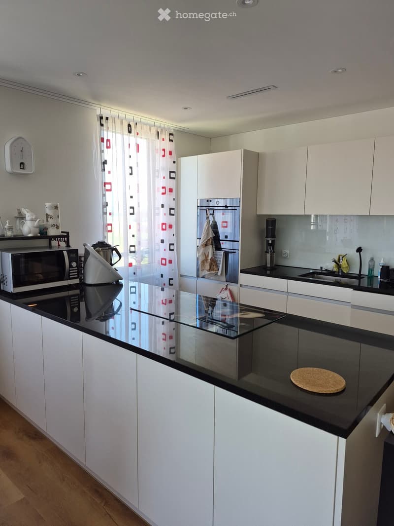 Modern kitchen with white cabinets, black countertops, and a glass island. Features a microwave, refrigerator, sink, and coffee maker.