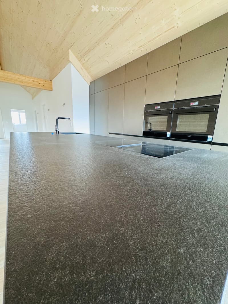 Large granite countertop, double oven, sink, faucet, wooden ceiling, white walls, tiled flooring
