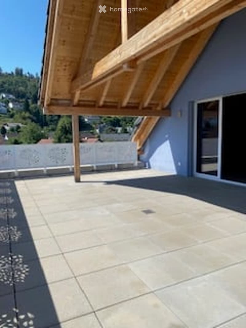 Balcony with wooden roof, tiled floor, white railing, and large window opening to the interior.
