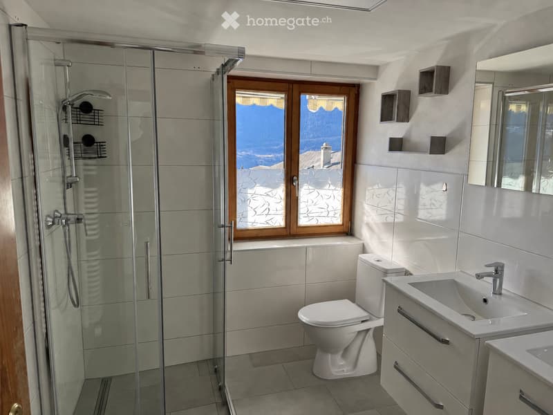 Modern bathroom with a glass-enclosed shower, toilet, sink, and a large window offering a scenic view.