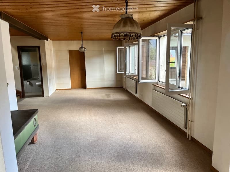 Empty room with carpeted floor, wooden ceiling, large windows, and a small cabinet visible on the left side.