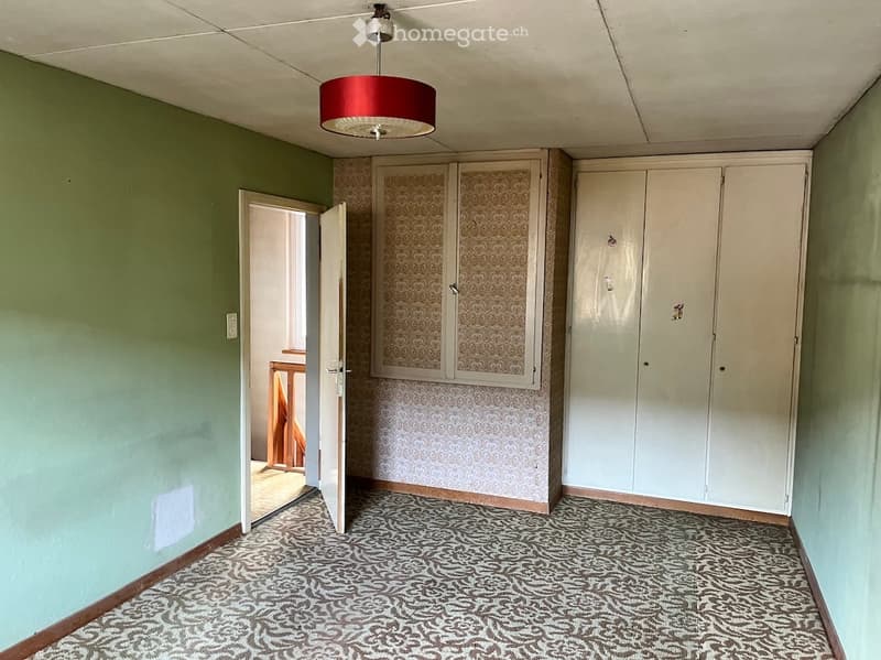 Empty room with light green walls, patterned carpet, white built-in wardrobes, and a red hanging light fixture.