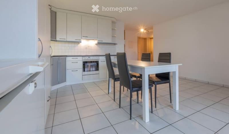 Bright, modern kitchen and dining area with white cabinets, a built-in oven, a refrigerator, and a white dining table with four black chairs.