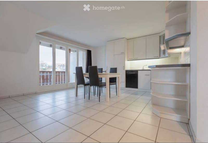 Bright, modern dining area with white tiled flooring, a dining table with four chairs, and a built-in kitchen featuring white cabinets and a dishwasher. Large windows and sliding doors lead to a balcony.