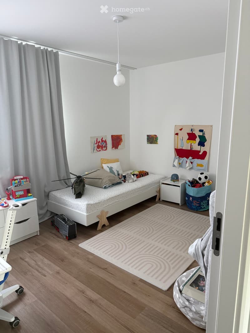 A child's bedroom with a single bed, pillows, toys, artwork, and a rug on the floor.