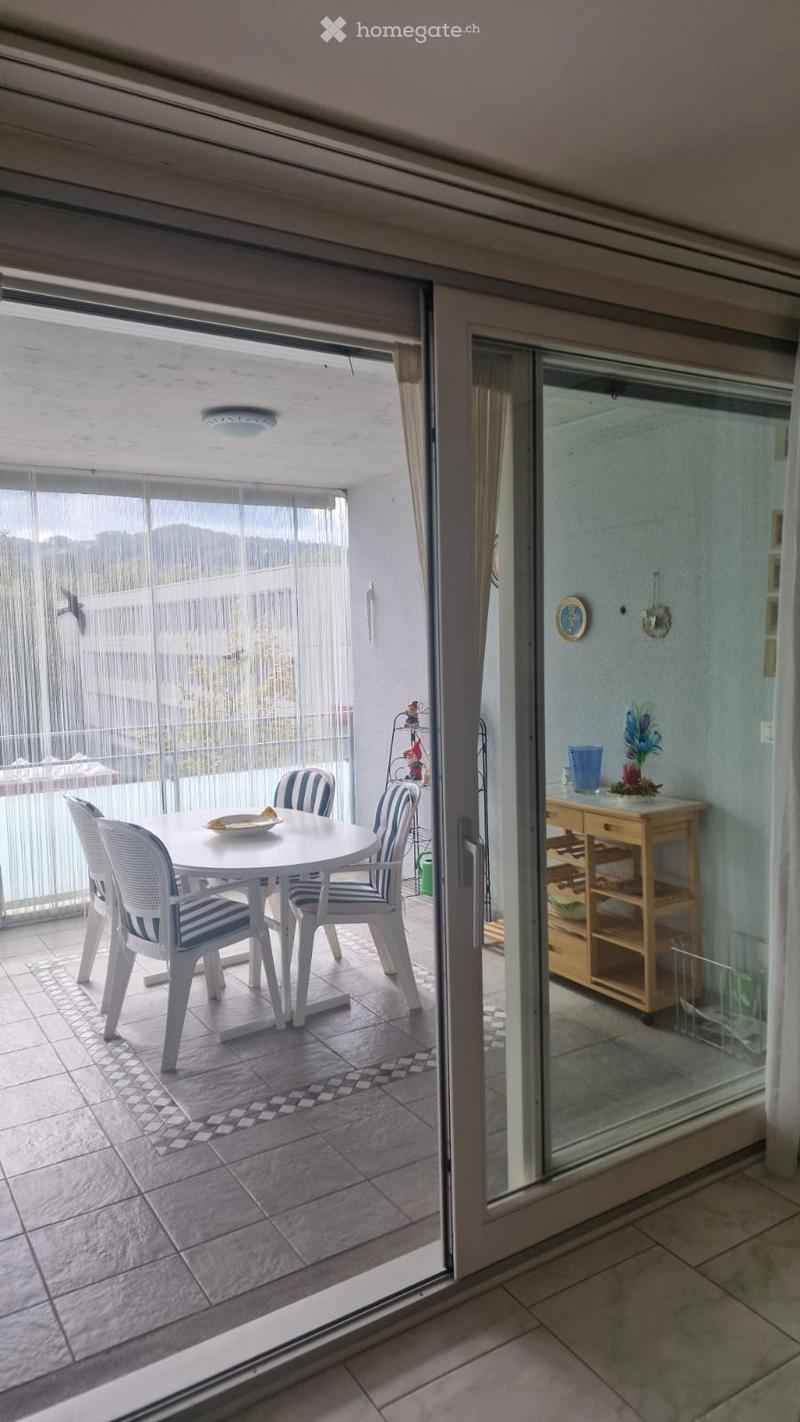 Balcony with a round table, four chairs, a small wooden cabinet with a flower pot, and a view of the outside area.