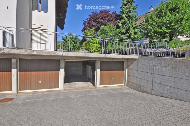 Multi-car garage with wooden doors, concrete walls, and a metal balcony railing above.
