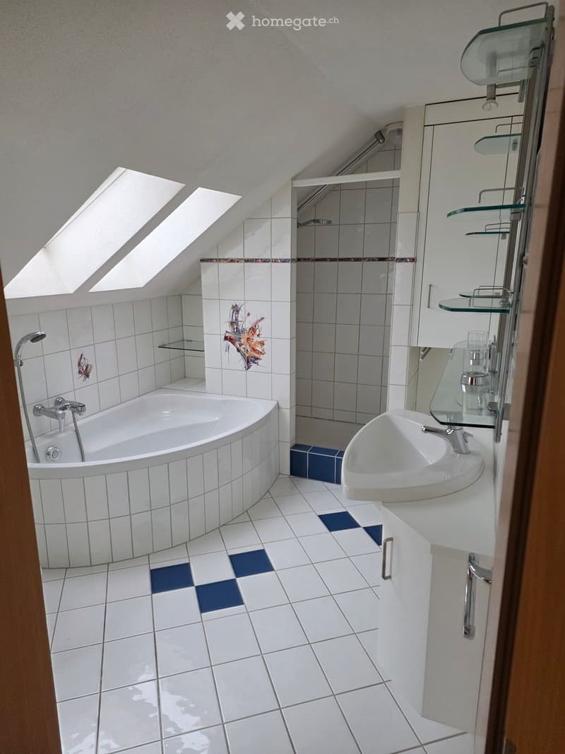 Modern bathroom with white tiled walls and floor, featuring a bathtub, sink, mirror, and glass shower enclosure. The room has skylight windows and decorative tiles.