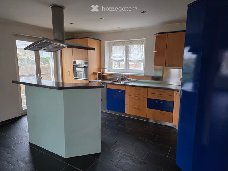 Modern kitchen with a central island, wooden cabinets, stainless steel appliances, and a black tiled floor.