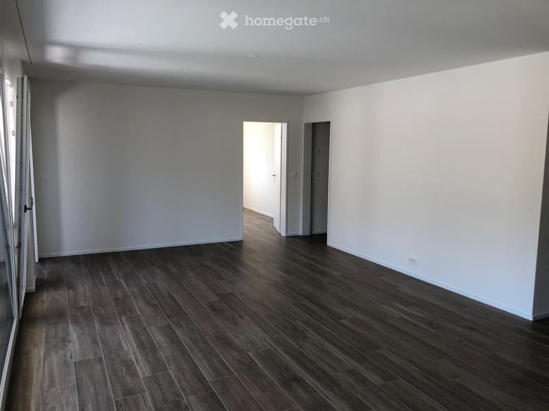 Empty room with wooden flooring, white walls, and two open doorways leading to other spaces.