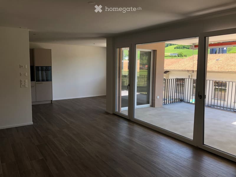 Empty room with wooden flooring, large sliding glass doors leading to a balcony, and white walls.