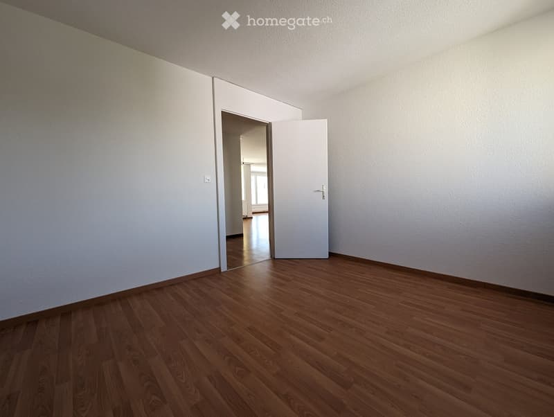 Empty room with wooden flooring and white walls, featuring a partially open white door leading to another room.