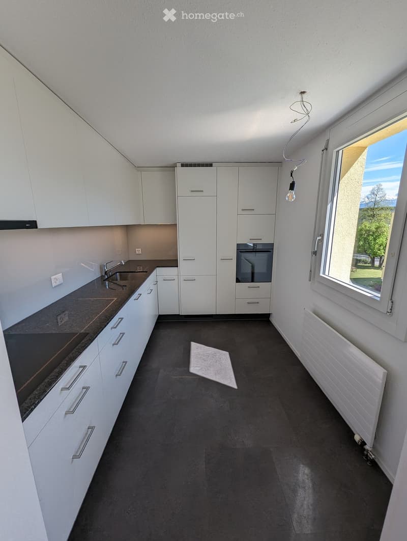 Modern kitchen with white cabinets, dark countertops, and a black floor. Features a sink, faucet, oven, and radiator.