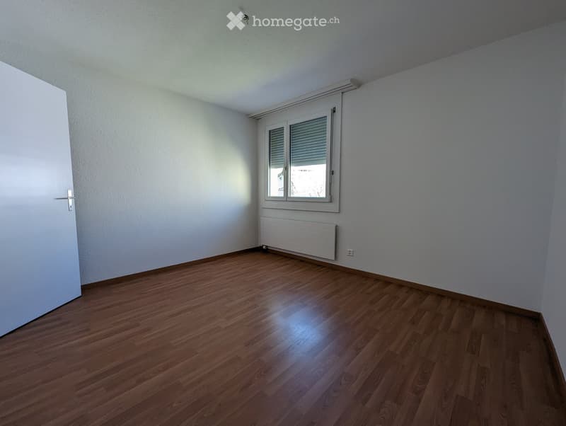 Empty room with wooden flooring, white walls, a window with blinds, and a radiator below the window.