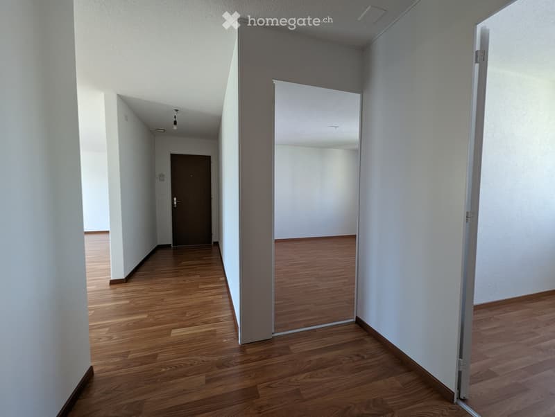 Empty hallway with wooden flooring, white walls, and a closed door at the end.