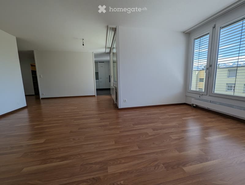 Empty room with wooden flooring, white walls, and large windows with blinds. No furniture or equipment is present.