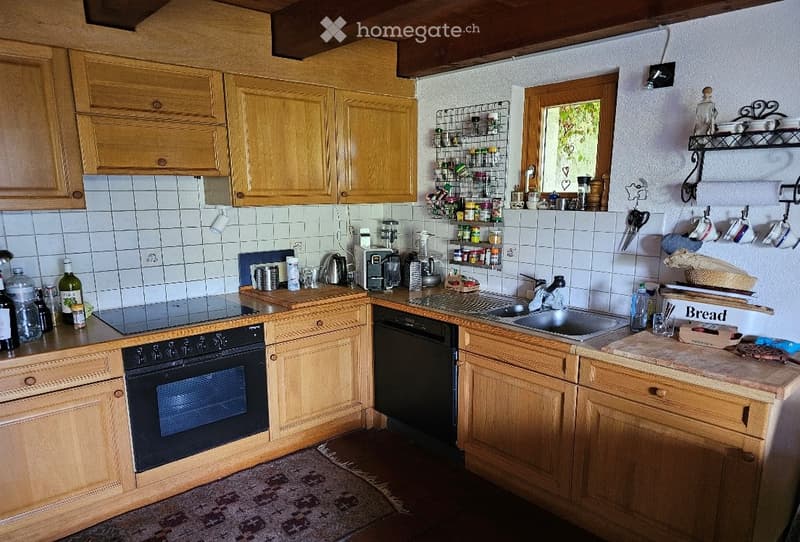 A cozy kitchen with wooden cabinets, a black oven, a dishwasher, a sink with a faucet, and a spice rack. The countertops are cluttered with various items, including bottles, cups, and a coffee maker.