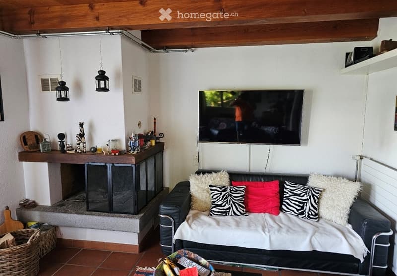 Living room with a black leather sofa, colorful throw pillows, a coffee table, a mounted TV, and a fireplace with decorative items on the mantel.