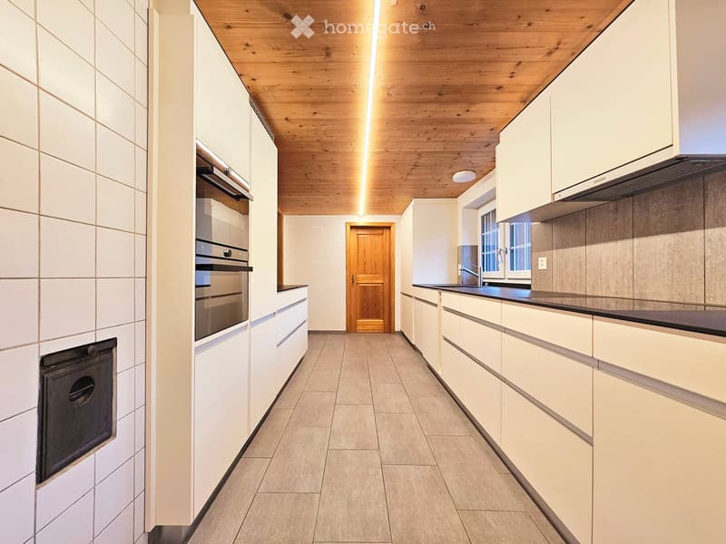 Modern kitchen with white cabinets, stainless steel appliances, and a wooden ceiling.