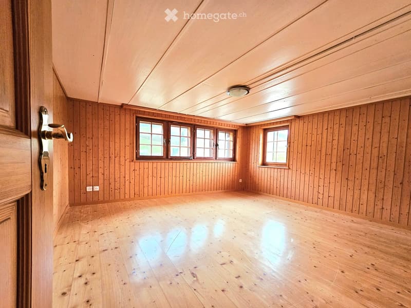 Empty room with wooden walls and floor, large windows, and a door.