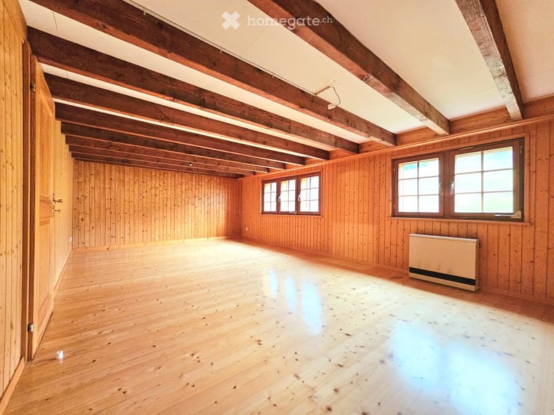 Empty room with wooden walls, wooden floor, exposed wooden beams on the ceiling, and multiple windows allowing natural light to enter.