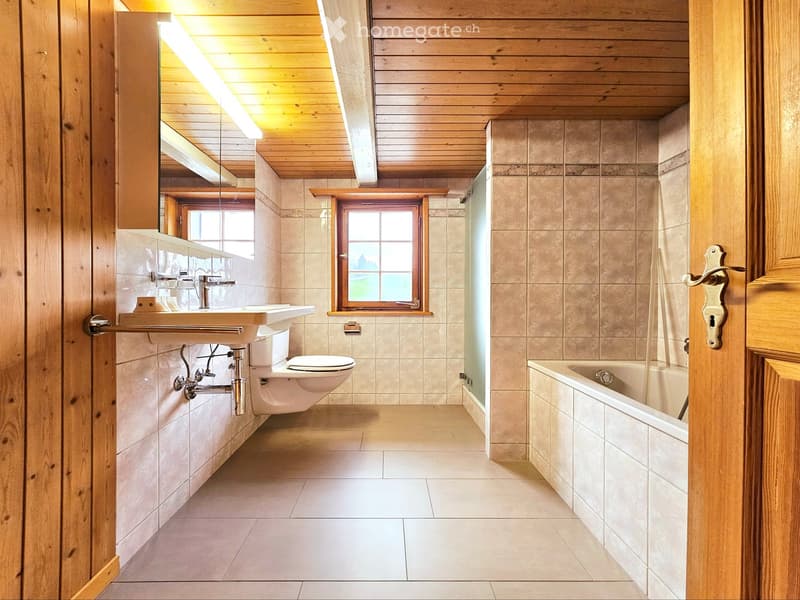 Bathroom with wooden ceiling, tiled walls, sink, toilet, bathtub, and a window providing natural light.