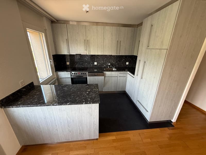 Modern kitchen with light wood cabinets, granite countertops, and stainless steel appliances including an oven, sink, and dishwasher.