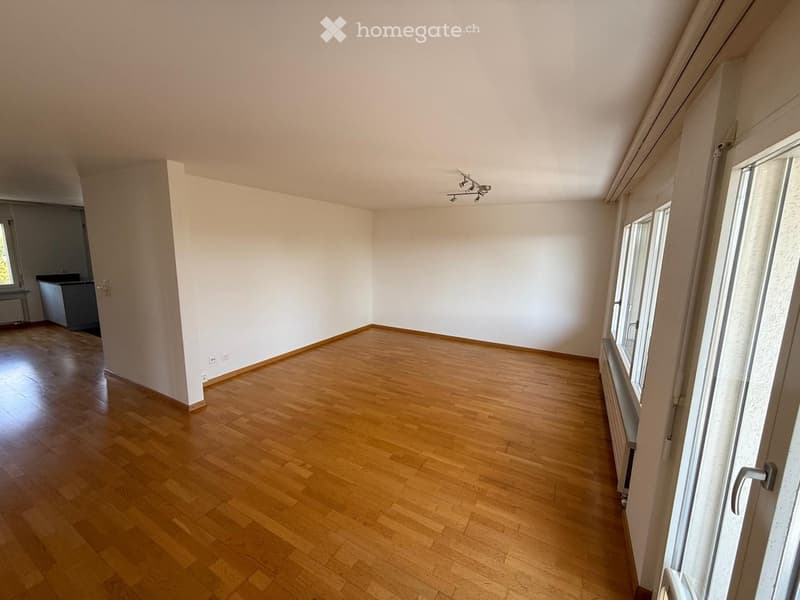 Empty room with wooden flooring, white walls, and large windows. No furniture or equipment visible.