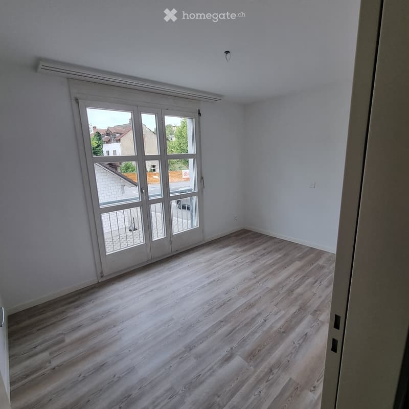 Empty room with light wooden flooring and white walls, featuring a large glass door leading outside.
