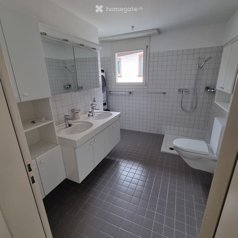 Modern bathroom with white tiles, a double sink, toilet, shower, and mirrored cabinet.