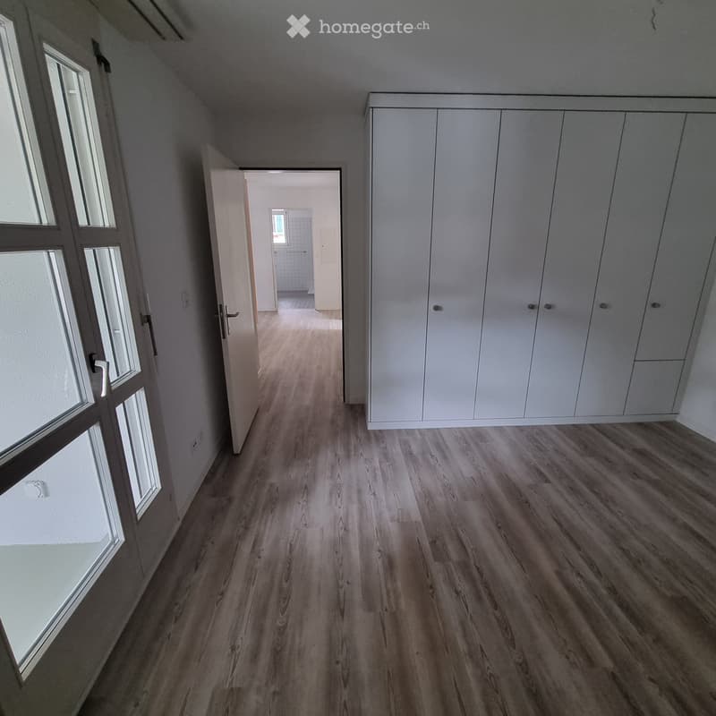 Empty hallway with wooden flooring, white walls, built-in white closet, and a door leading to another room.
