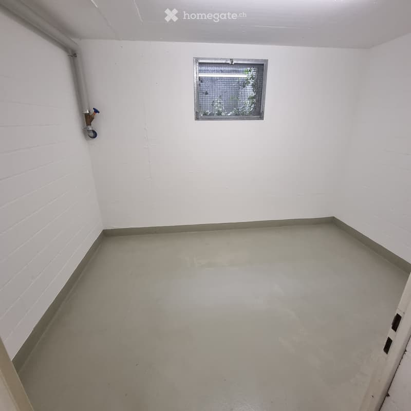 Empty room with white brick walls, concrete floor, and a small window with a metal frame. A water tap is visible on the left wall.