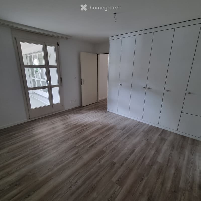 Empty room with wooden flooring, white walls, large sliding glass door, and built-in white wardrobe.