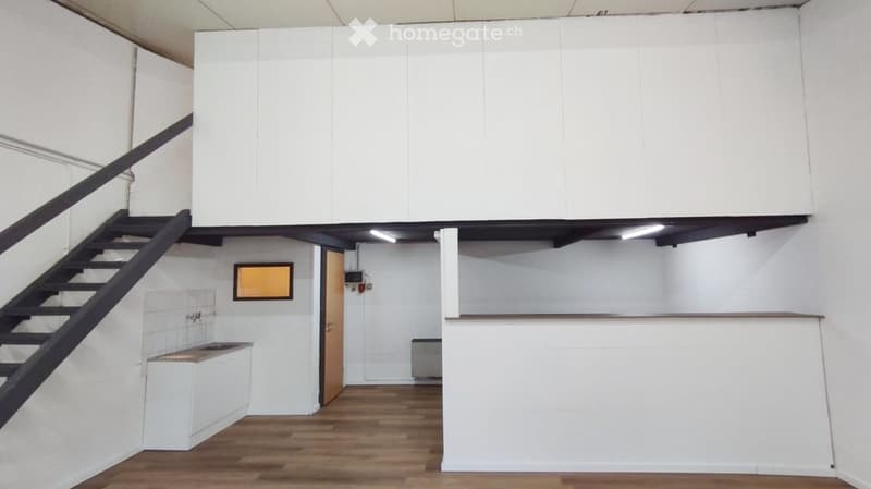 Empty room with white walls, wooden floor, staircase leading to a loft area, and a small sink area.