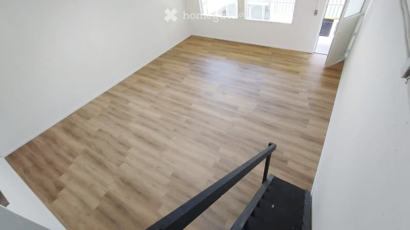 Empty room with light wooden flooring, white walls, and large windows. No furniture or equipment present.