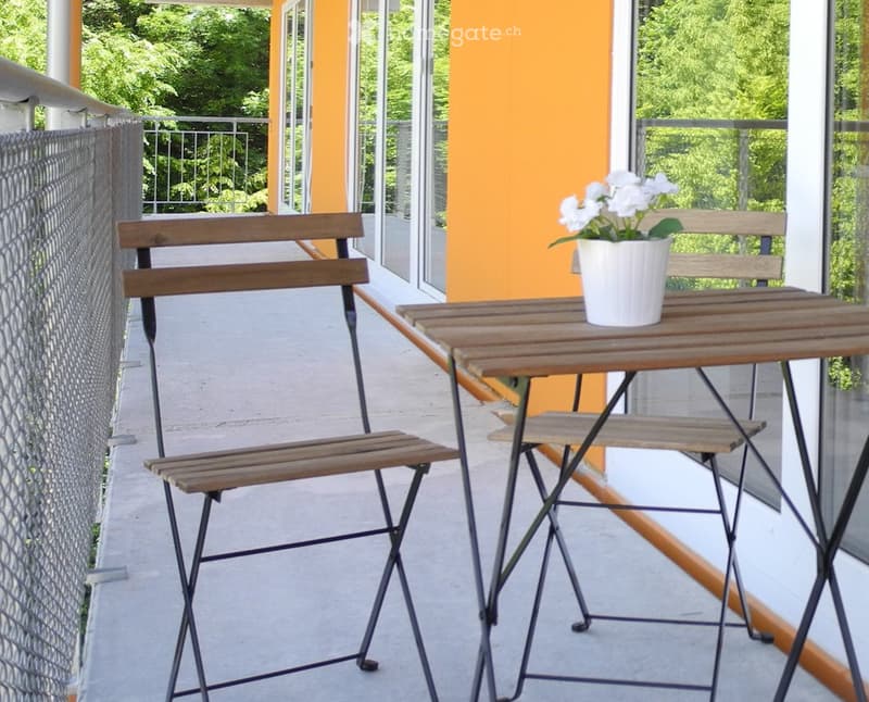 Balcony with a small wooden table, two folding chairs, and a white flower pot on the table.
