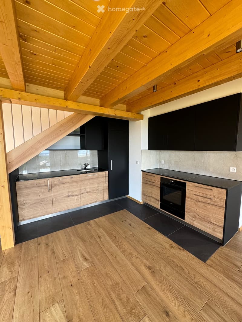 Modern kitchen with wooden beams, black countertops, and stainless steel appliances. Features include a sink, oven, and wooden cabinets.