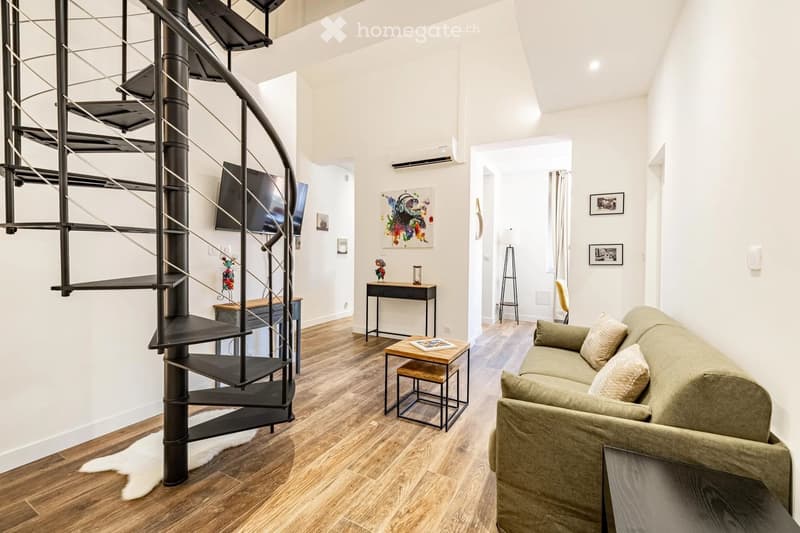 Modern living room with a spiral staircase, sofa, coffee table, small table, and television mounted on the wall.