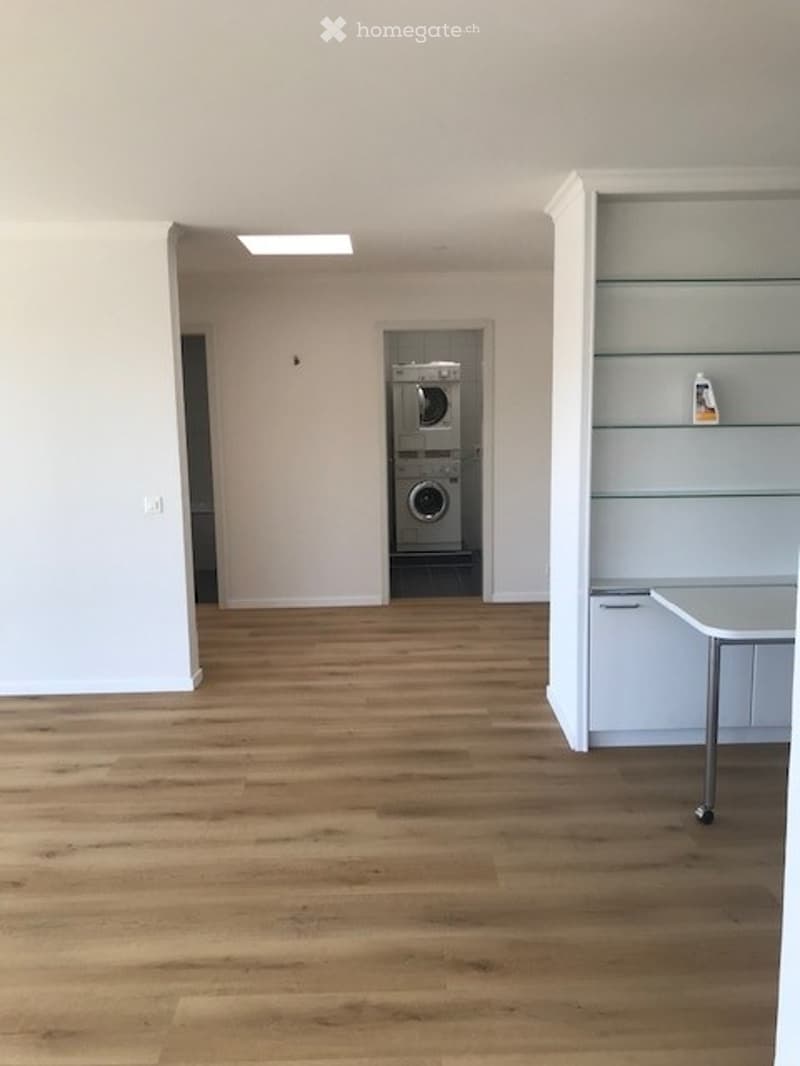 Empty room with wooden flooring, white walls, and a private washing machine in the corner.