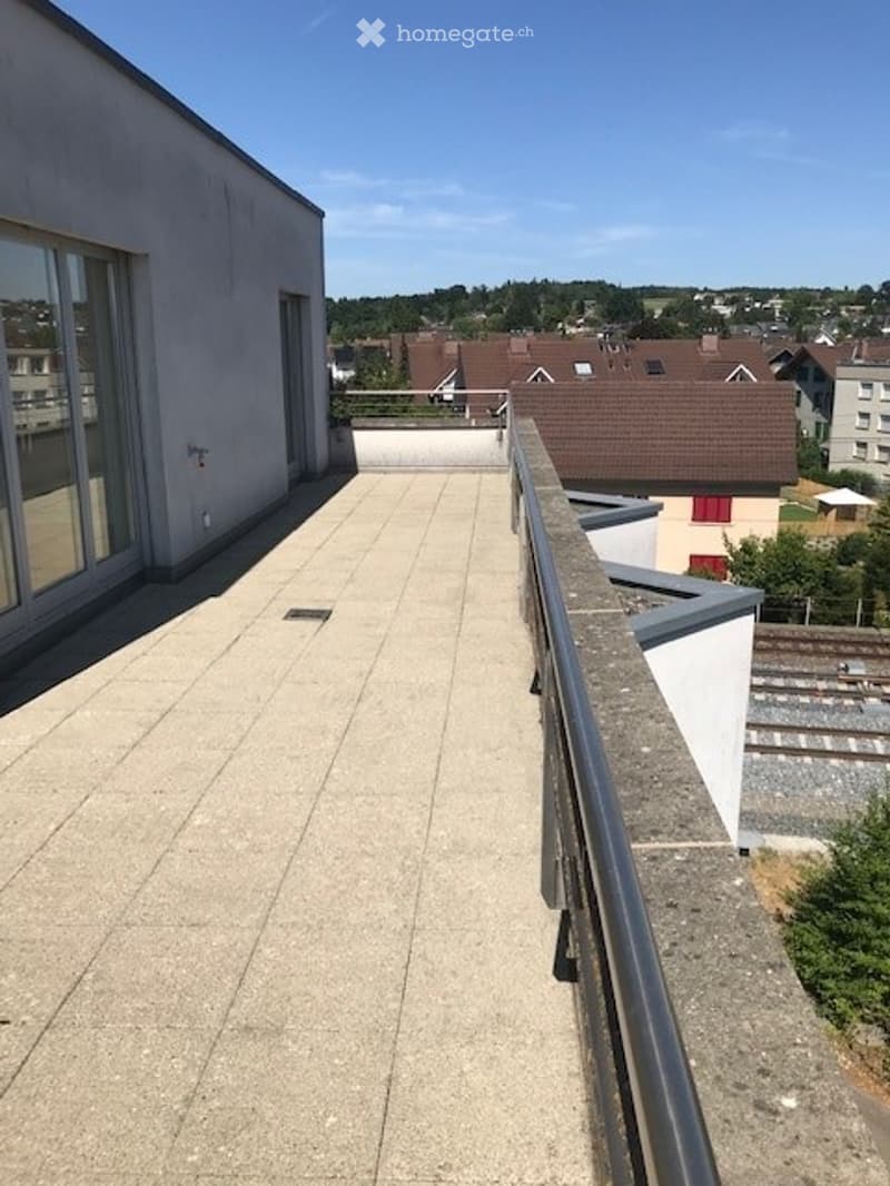 Balcony with concrete floor, metal railing, and a view of the surrounding area including houses and greenery.