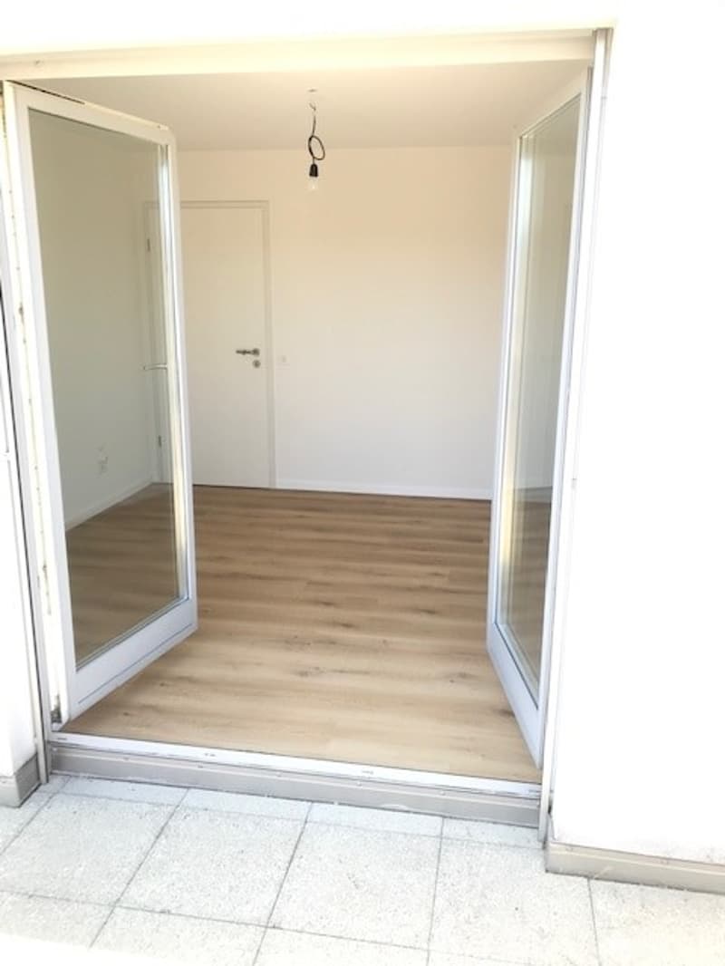 Empty room with wooden flooring, white walls, and large glass doors leading to a tiled area.