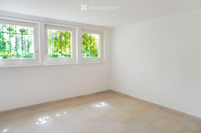 Empty room with white walls, tiled floor, and three windows with green views outside.