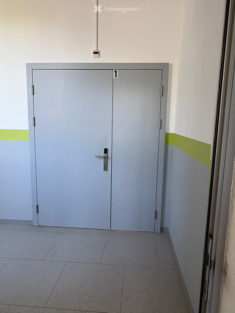 Empty hallway with a grey double door marked '1', light grey tiled floor, and white walls with a green accent stripe.